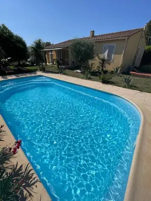 a blue swimming pool in front of a house at Maison de vacances in Le Thor