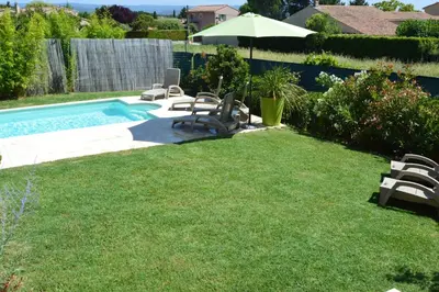 a yard with a pool with chairs and an umbrella at les lauriers in Caromb