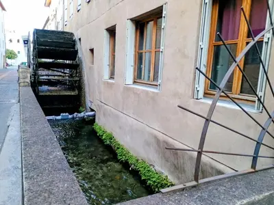 a building next to a river next to a building at Spacieux 74 m2 Standing Clim & Parking Privé Centre Ville in LʼIsle-sur-la-Sorgue