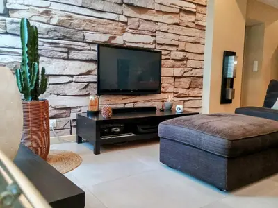 a living room with a tv on a stone wall at Spacieux 74 m2 Standing Clim & Parking Privé Centre Ville in LʼIsle-sur-la-Sorgue
