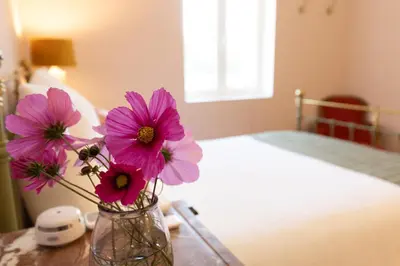 a vase with pink flowers on a table next to a bed at Terres Élaïs in Robion en Luberon