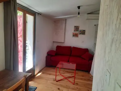 a living room with a red couch and a table at Petit studio avec jardin à 10 mn d'Avignon in Entraigues-sur-la-Sorgue