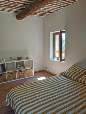 a white bedroom with a striped bed and a window at Trés jolie bastidon de village in Puyvert