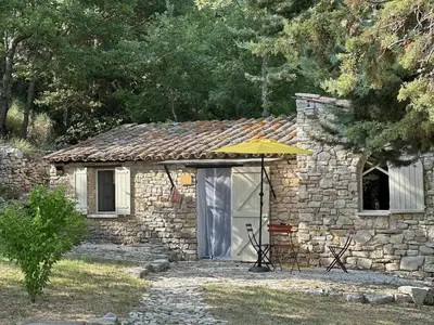 a stone house with an umbrella and a table and chairs at Le Bastidon in Caseneuve