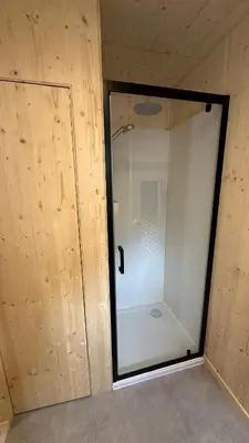 a glass shower door in a room with a wooden wall at Cabane dans le Luberon - Bird in Provence in Cavaillon