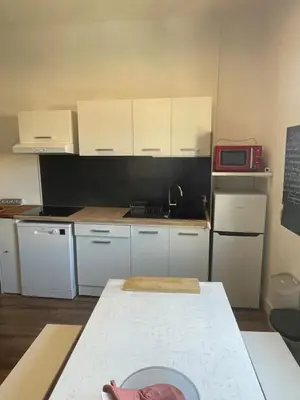 a small kitchen with white cabinets and a table at Studio climatisé au centre du village in Saint-Michel-lʼObservatoire