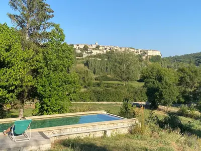 a person sitting in a chair next to a swimming pool at Le Pré de la Reyne in Sault-de-Vaucluse