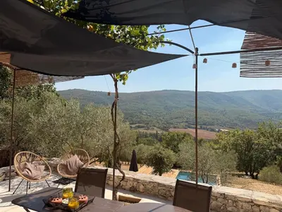 a patio with a table and chairs and an umbrella at Bastidon avec vue et piscine au coeur du Luberon in Céreste