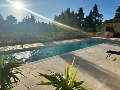 a swimming pool in a backyard with the sun shining at Le Jas de la Cascade in Les Vignères