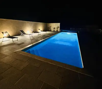 a swimming pool at night with chairs and lights at Le Jas de la Cascade in Les Vignères