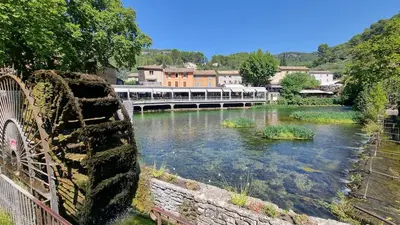 a river with a train traveling over a bridge at La Cour de Pétrarque in Fontaine-de-Vaucluse