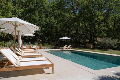 a swimming pool with chairs and umbrellas next to a swimming pool at Spacious villa in Provence in Le Puy-Sainte-Réparade