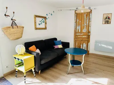 a living room with a black couch and a table at Havre de paix proche centre ville, jardin, piscine in LʼIsle-sur-la-Sorgue