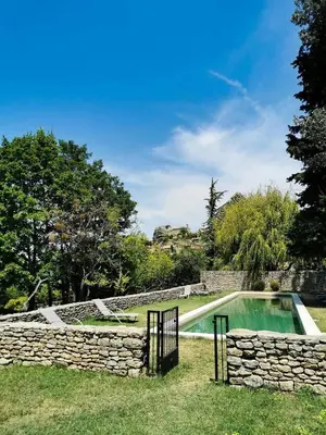 a swimming pool in a stone wall next to a yard at Auberge du Presbytère in Saignon