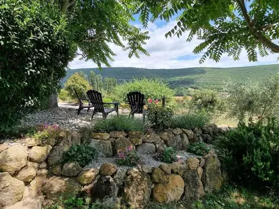 two chairs and a table in a garden with a rock wall at Gîtes de la Coupière Le Laurier in Aubenas-les-Alpes