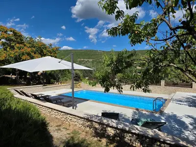 a swimming pool with a white umbrella and chairs at Gîtes de la Coupière Le Laurier in Aubenas-les-Alpes