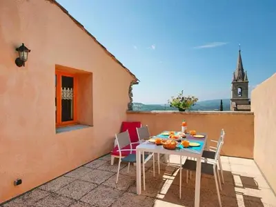 a table and chairs on a balcony with a clock tower at Apartment Morard - Bonnieux Appt 2- Etage by Interhome in Bonnieux