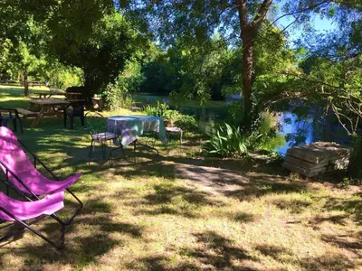 a picnic table and chairs in a yard next to a pond at Le Castor et La Loutre - Gites en bord de Sorgue in LʼIsle-sur-la-Sorgue