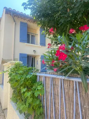 a house with blue windows and a fence with pink flowers at La Cigale Bleue in Villes-sur-Auzon