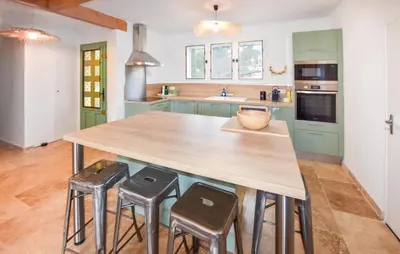 a kitchen with green cabinets and a wooden island with stools at Maison Avec Piscine Privée in Mazan