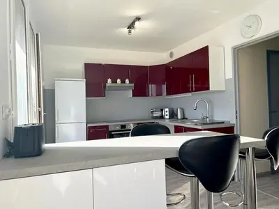 a kitchen with red cabinets and a counter with chairs at Appartement Spacieux avec Balcon in Carpentras
