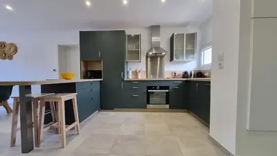 a large kitchen with green cabinets and a table at Villa Quercus Design Piscine et Loisirs in Ménerbes