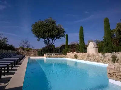 a swimming pool with benches and a stone wall at Le Mazet du Domaine in Gordes