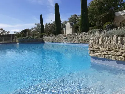 a swimming pool with blue water and a stone wall at Le Mazet du Domaine in Gordes