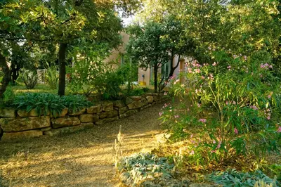a garden with a stone wall and trees and flowers at La Rousse in Roussillon
