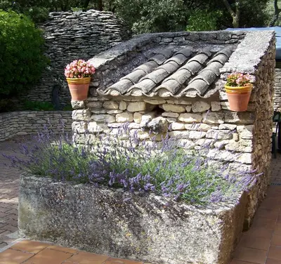 a stone wall with two flower pots and purple flowers at Le Verger in Gordes