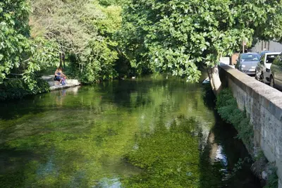 a person sitting on a bench next to a river at Colombe in LʼIsle-sur-la-Sorgue