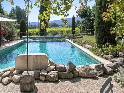 a pool in a yard with a chair and rocks at Maison charmante à Oppède avec piscine partagée in Oppède