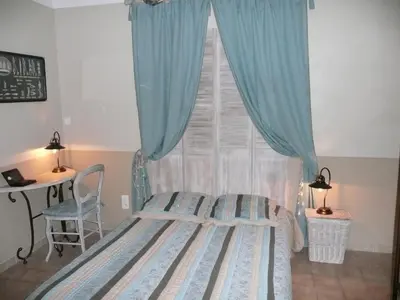 a bedroom with a bed and a window with blue curtains at Mas les vieux chênes in Lambesc