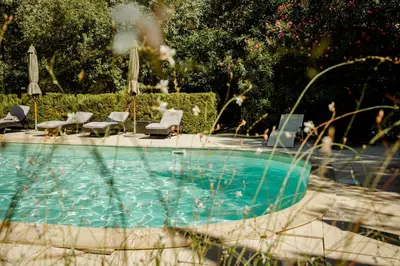 a blue swimming pool with chairs and umbrellas at Le Mas de Trévouse in Saint-Saturnin-lès-Avignon