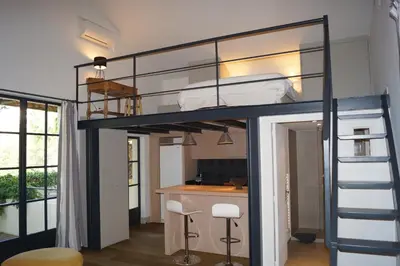 a loft bed in a room with a kitchen and a desk at Domaine de la Girafe in Eyragues