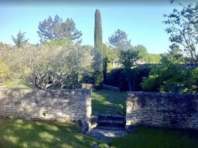 a garden with a stone wall and a monument at Le Petit Bastidon - Private pool - Gordes in Gordes