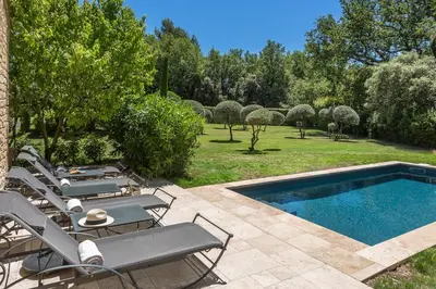 a backyard with a swimming pool and chairs and trees at Domaine Les Roullets in Oppède