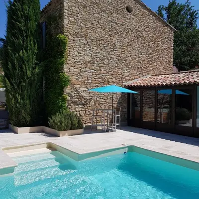a swimming pool with an umbrella next to a house at Le Mas Vigneron in Gordes