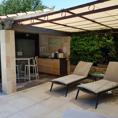 a patio with a pergola and chairs and a kitchen at Le Mas Vigneron in Gordes