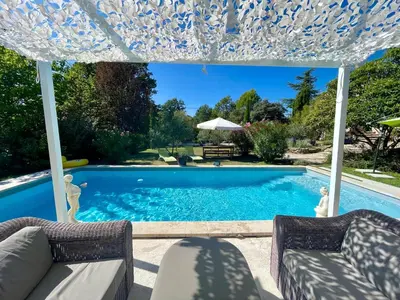 a swimming pool with two chairs and an umbrella at La belle histoire Gîte Ventoux in Bédoin