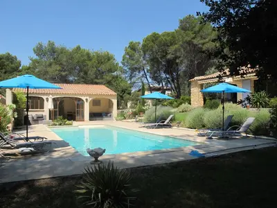 a swimming pool with two blue umbrellas and chairs at L'Oustau de Bigatié in Lambesc