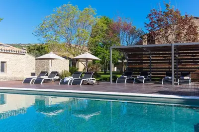 a swimming pool with lounge chairs and umbrellas next to at Hôtel Carcarille Restaurant Le C in Gordes