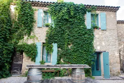 a stone building with blue shutters and a bench in front at La Belugue in Beaumont-de-Pertuis