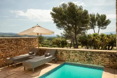 a pool with two chairs and an umbrella next to a stone wall at Le Phébus & Spa – Relais & Châteaux in Joucas
