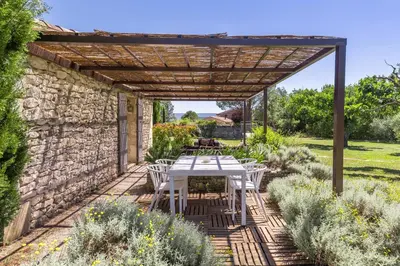 a patio with a table and chairs under a wooden pergola at Mas Oréa côté piscine in Gordes