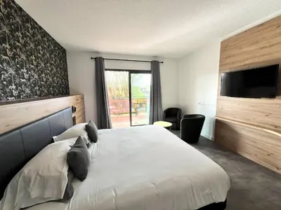 a bedroom with a bed and a tv and a window at Hotel Les Nevons in LʼIsle-sur-la-Sorgue