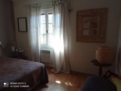 a bedroom with a bed and a window and a chair at La Maison de Maïté in Cheval-Blanc