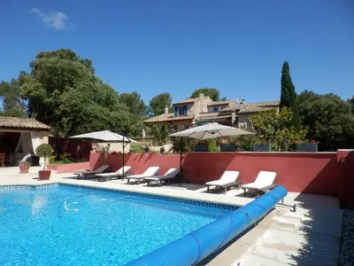 a pool with chairs and umbrellas next to a house at Gite Le city en Provence in Lambesc