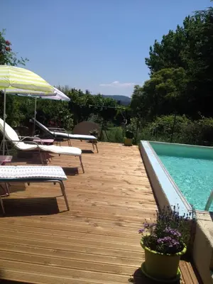 a wooden deck with a pool and chairs and an umbrella at L'Oustalet in La Tour-dʼAigues
