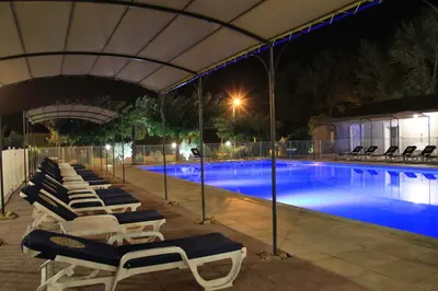a group of lounge chairs and a swimming pool at night at Hôtel Saint Louis in Le Thor